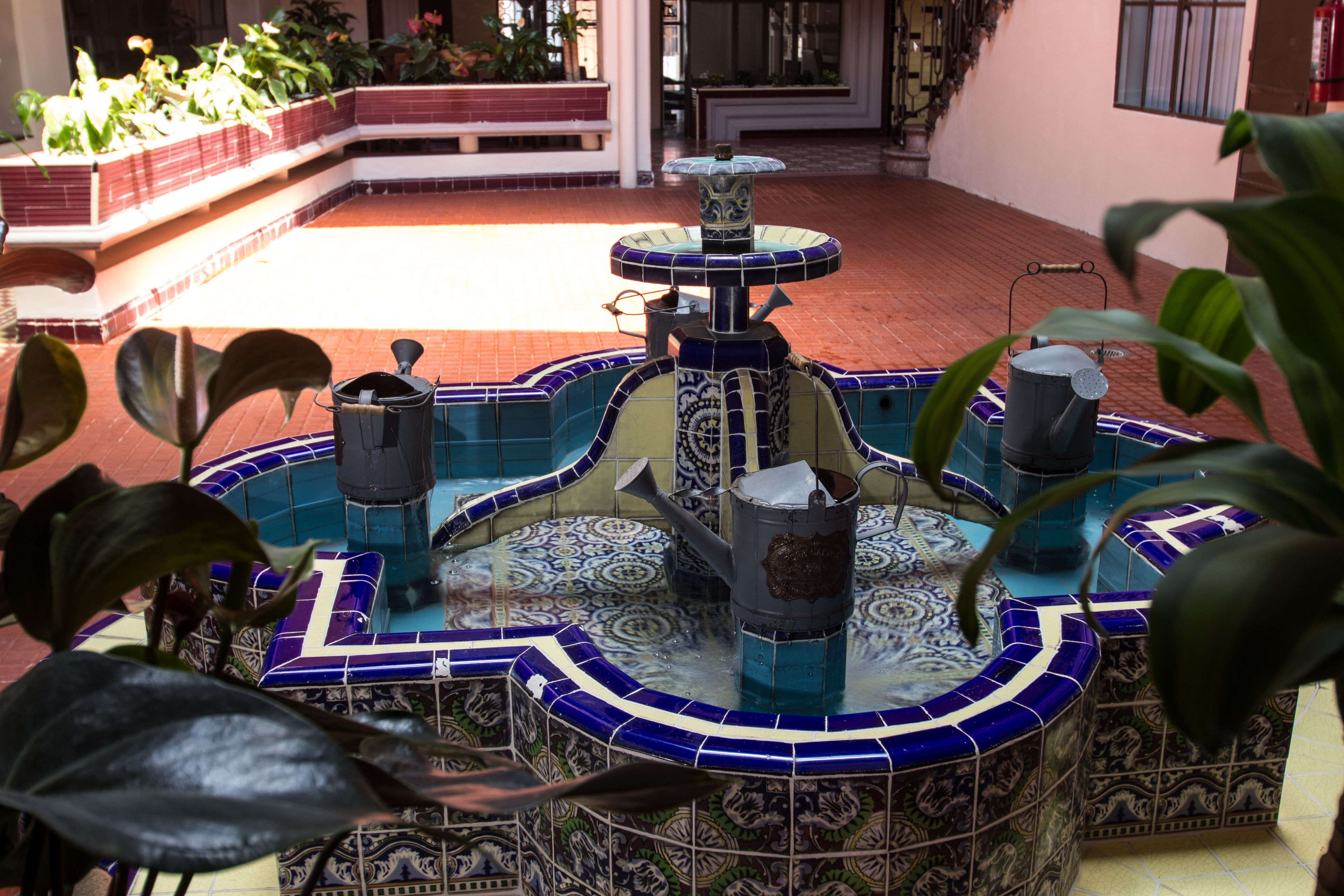 A decorative fountain with multiple tiers and a tiled base, surrounded by potted plants.