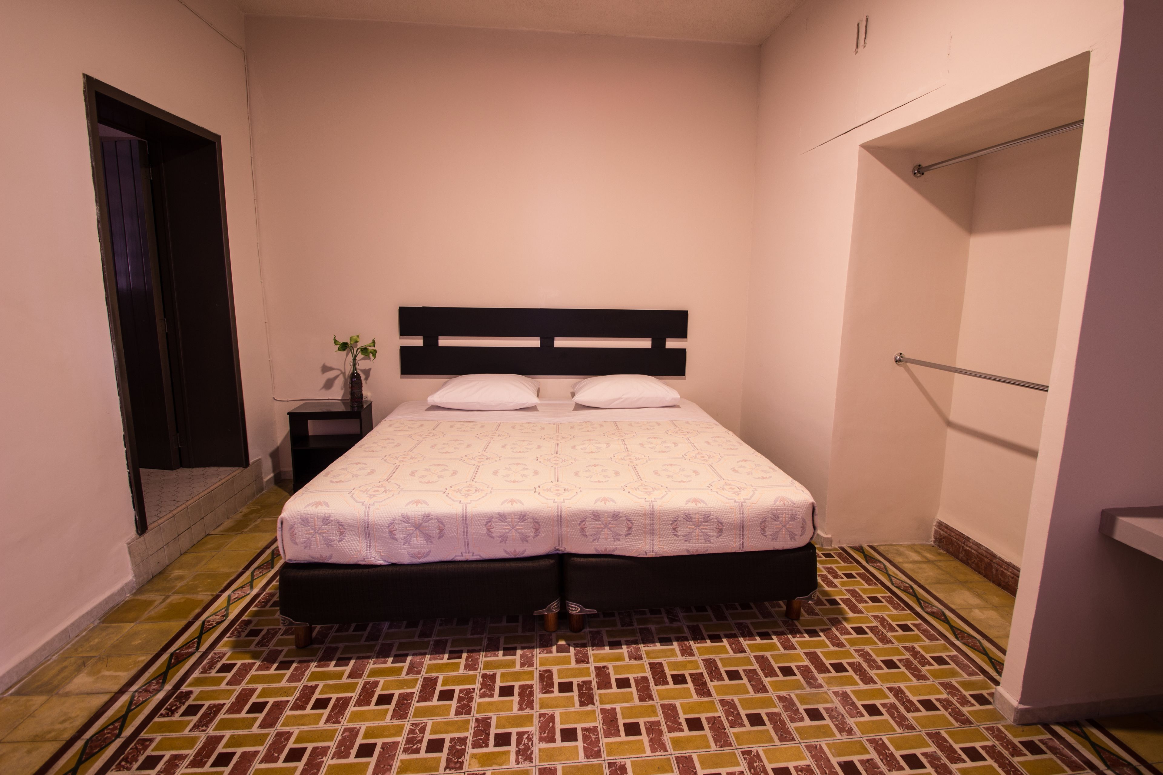 A small, neatly arranged bedroom with a single bed, a nightstand, and a small table with a plant.