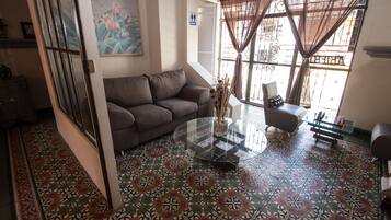 Uma sala de estar com piso estampado, um sofá, uma mesa de centro de vidro e uma poltrona.