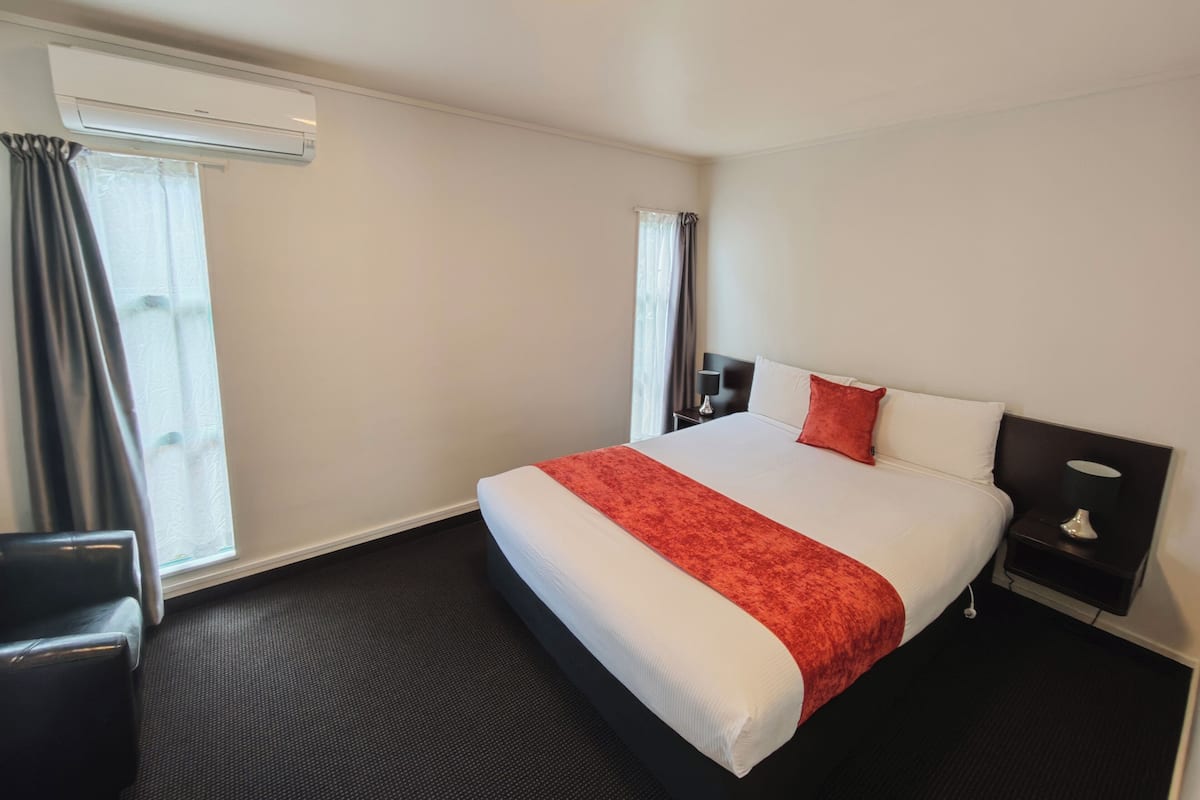 Une chambre d’hôtel avec un grand lit, une table de chevet avec une lampe, une chaise et un appareil de climatisation.