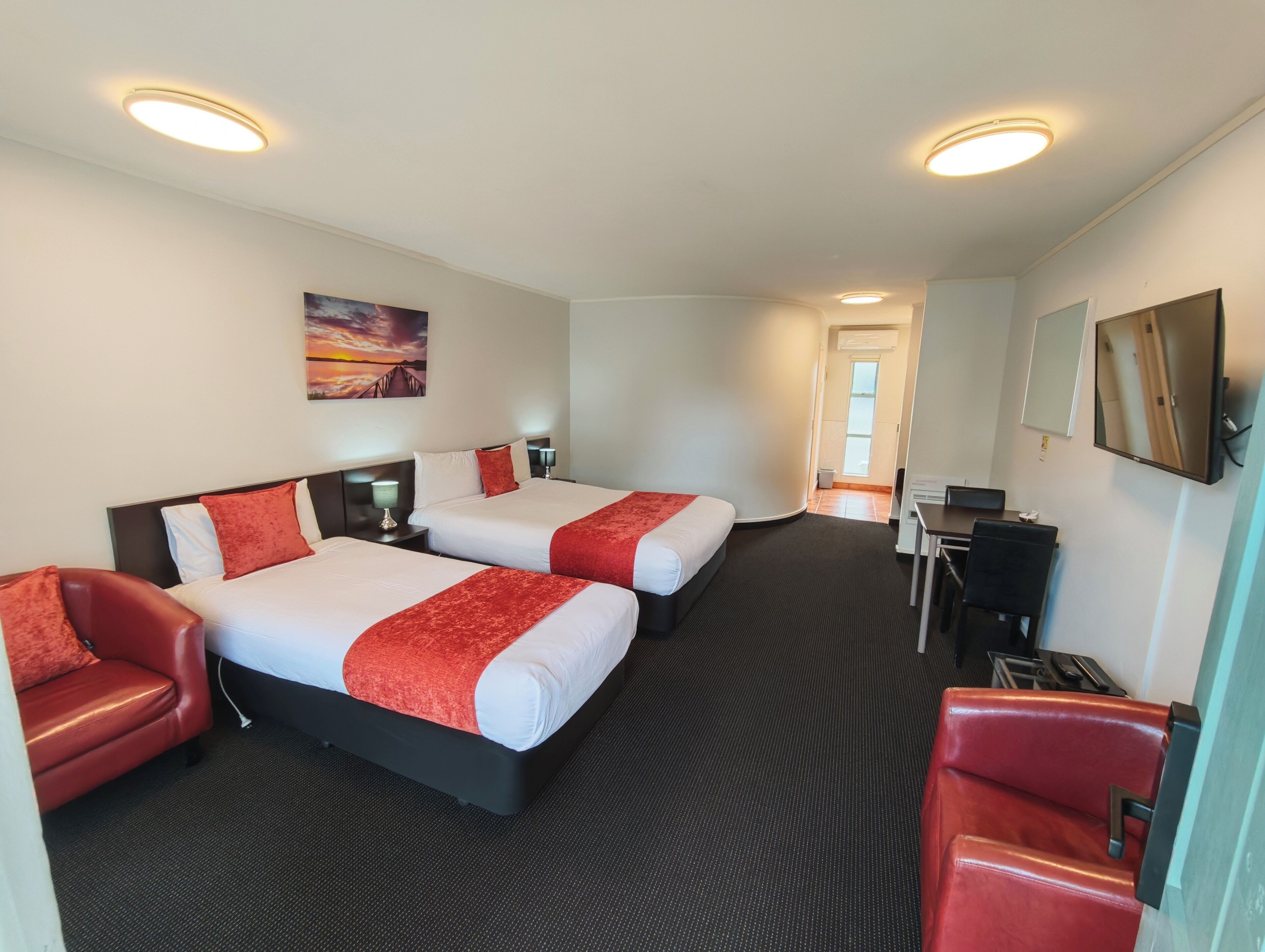 A hotel room with two beds, a desk, a chair, and a TV.