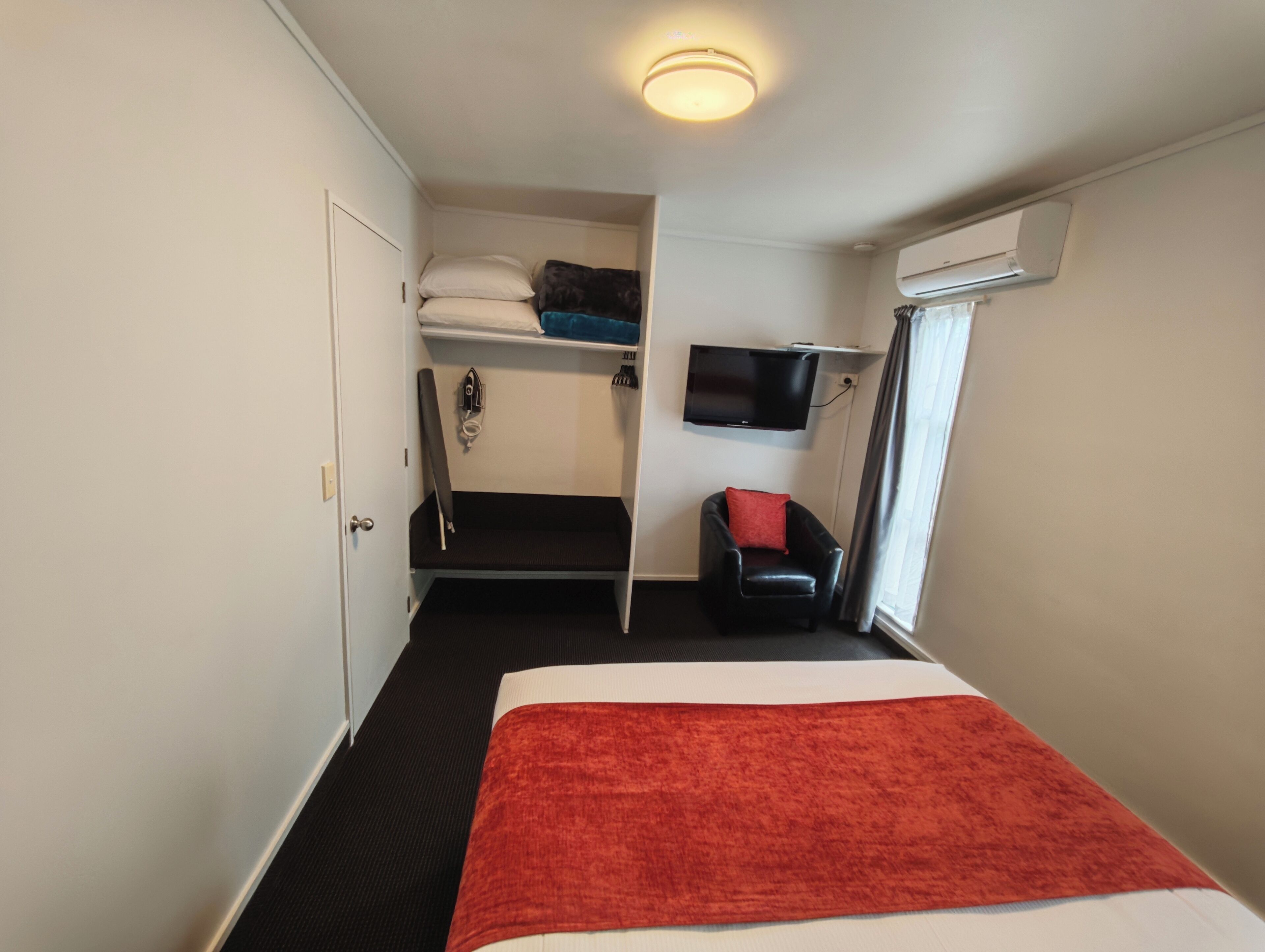 A compact hotel room with a bed, a small seating area, a TV, and a window.