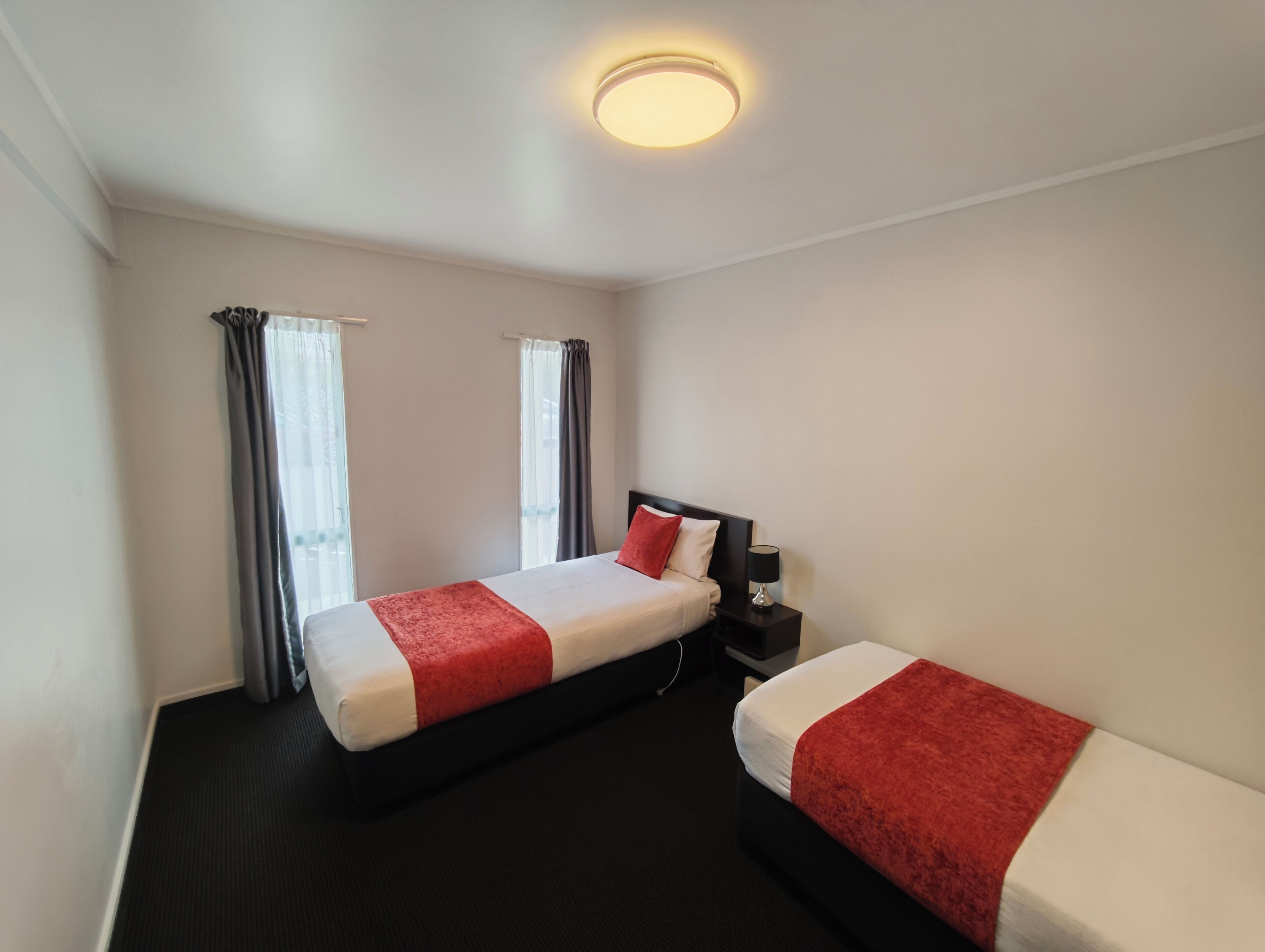 Een hotelkamer met twee bedden, een nachtkastje, een lamp en een plafondlamp.