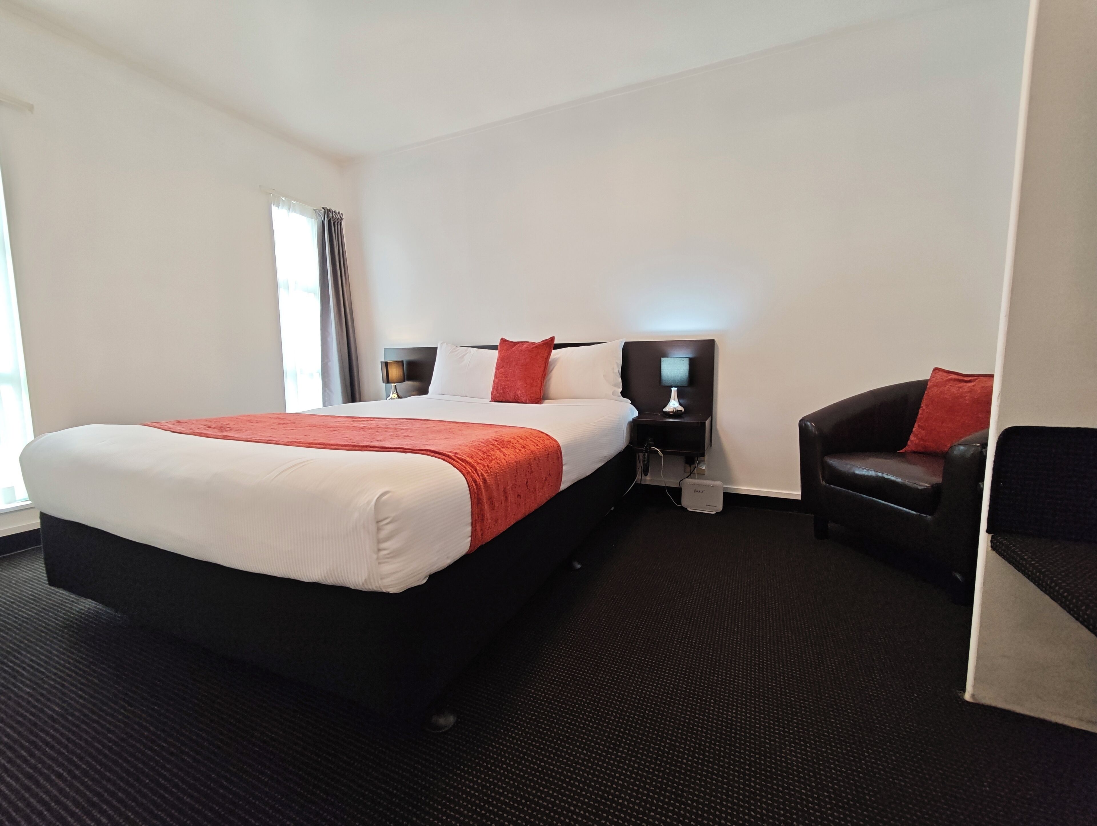 A hotel room with a large bed, two bedside tables, a chair, and a window with curtains.