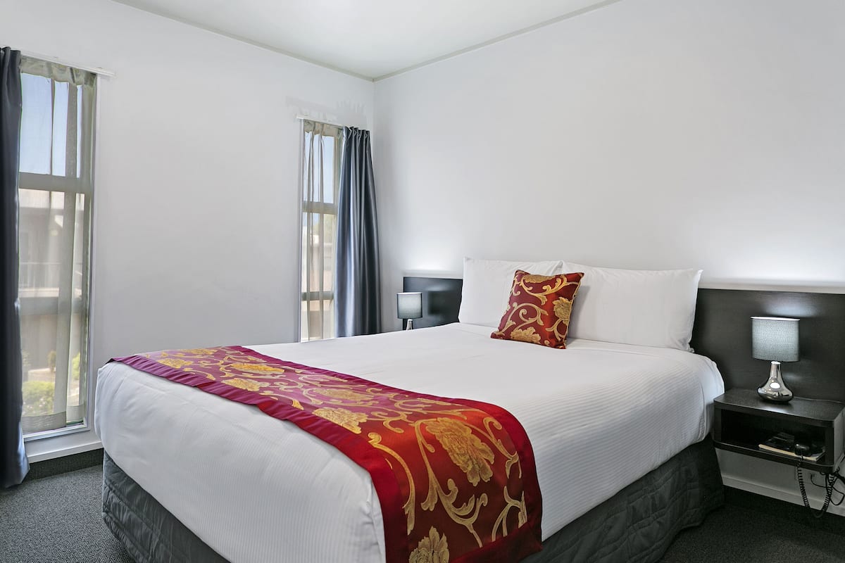 Une chambre d’hôtel avec un grand lit, deux tables de chevet avec des lampes, une fenêtre avec des rideaux et une vue sur l’extérieur.