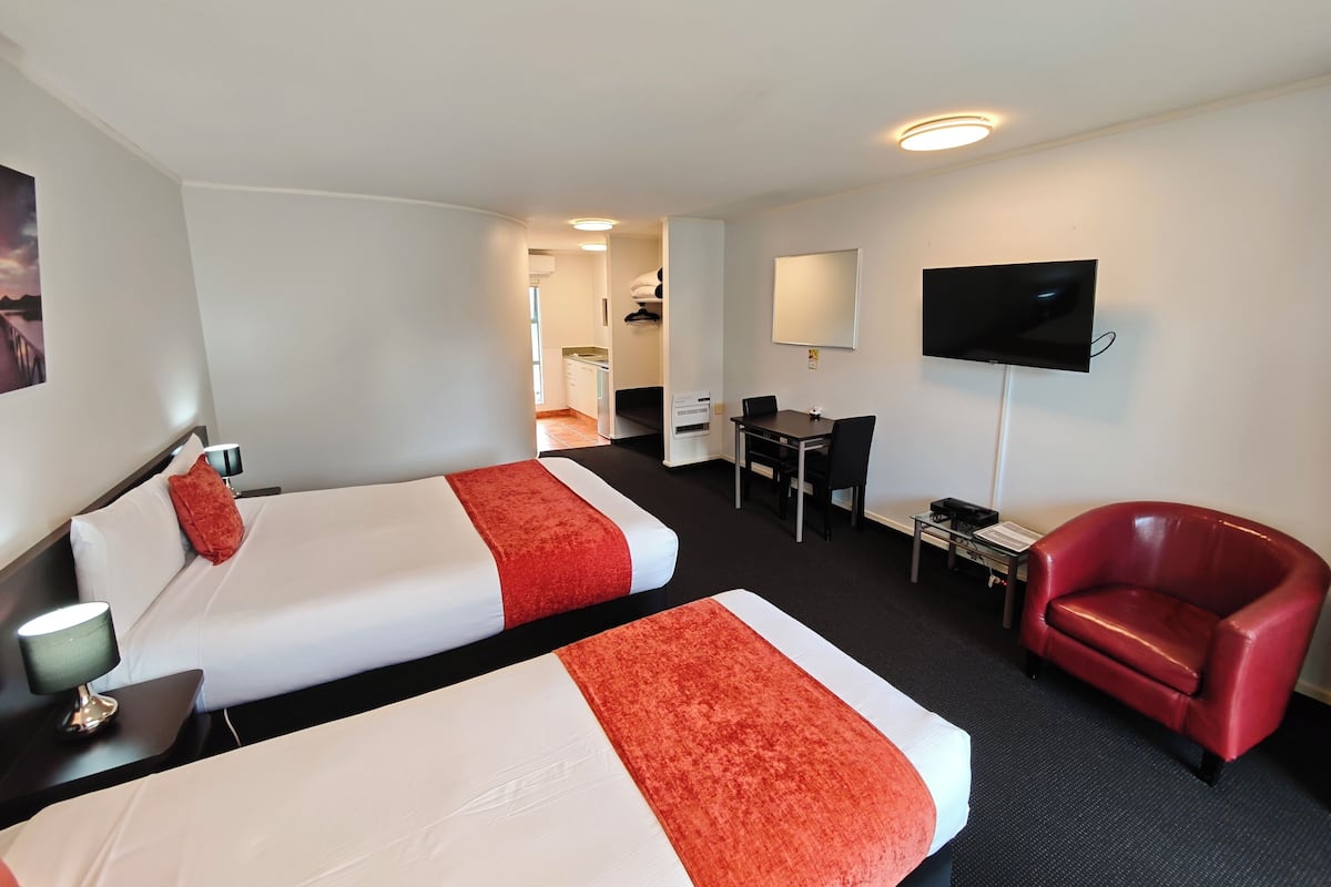 Une chambre d’hôtel avec deux lits, un bureau, une télévision et une chaise rouge.