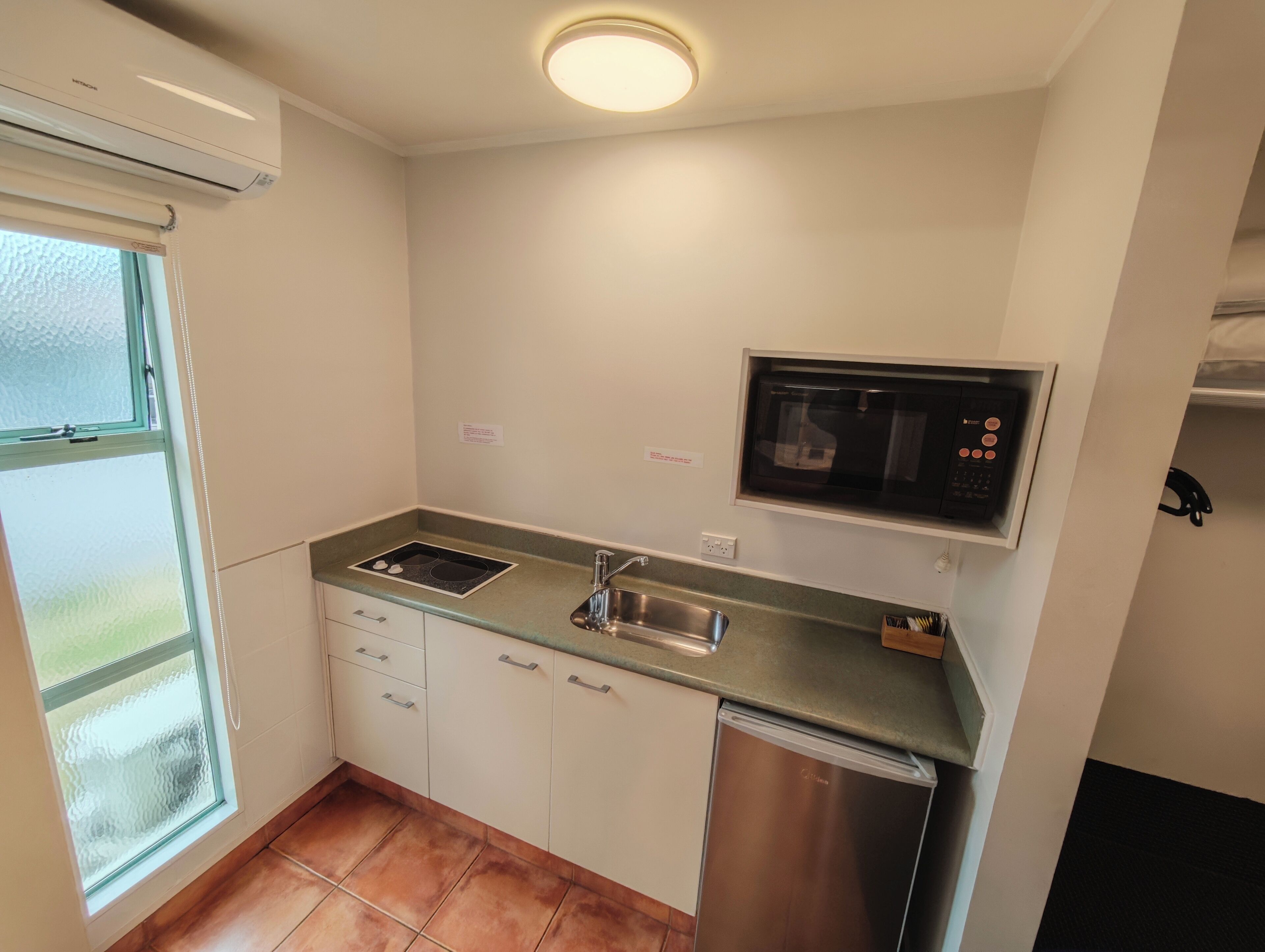 A compact kitchen with a built-in microwave, a stainless steel refrigerator, and a window with frosted glass.