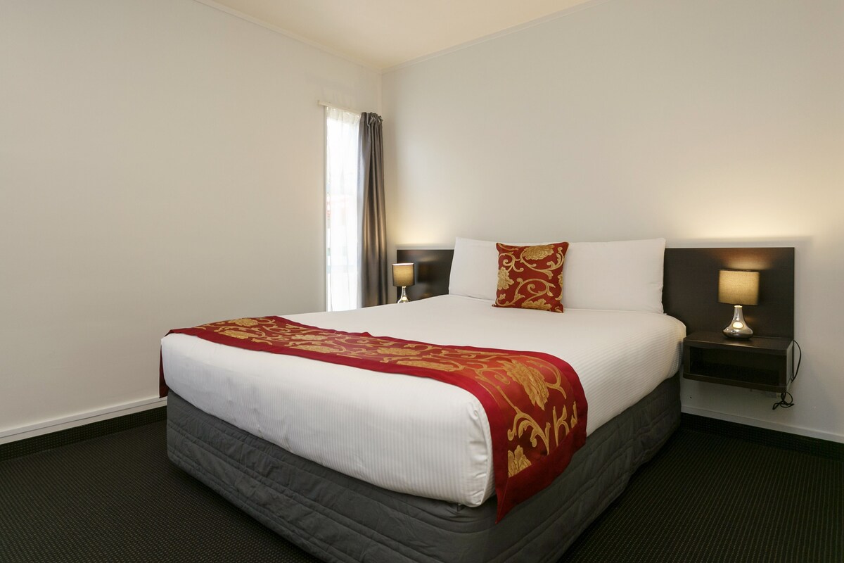 Een hotelkamer met een groot bed, twee nachtkastjes met lampen, een raam met gordijnen en een vloerbedekking.