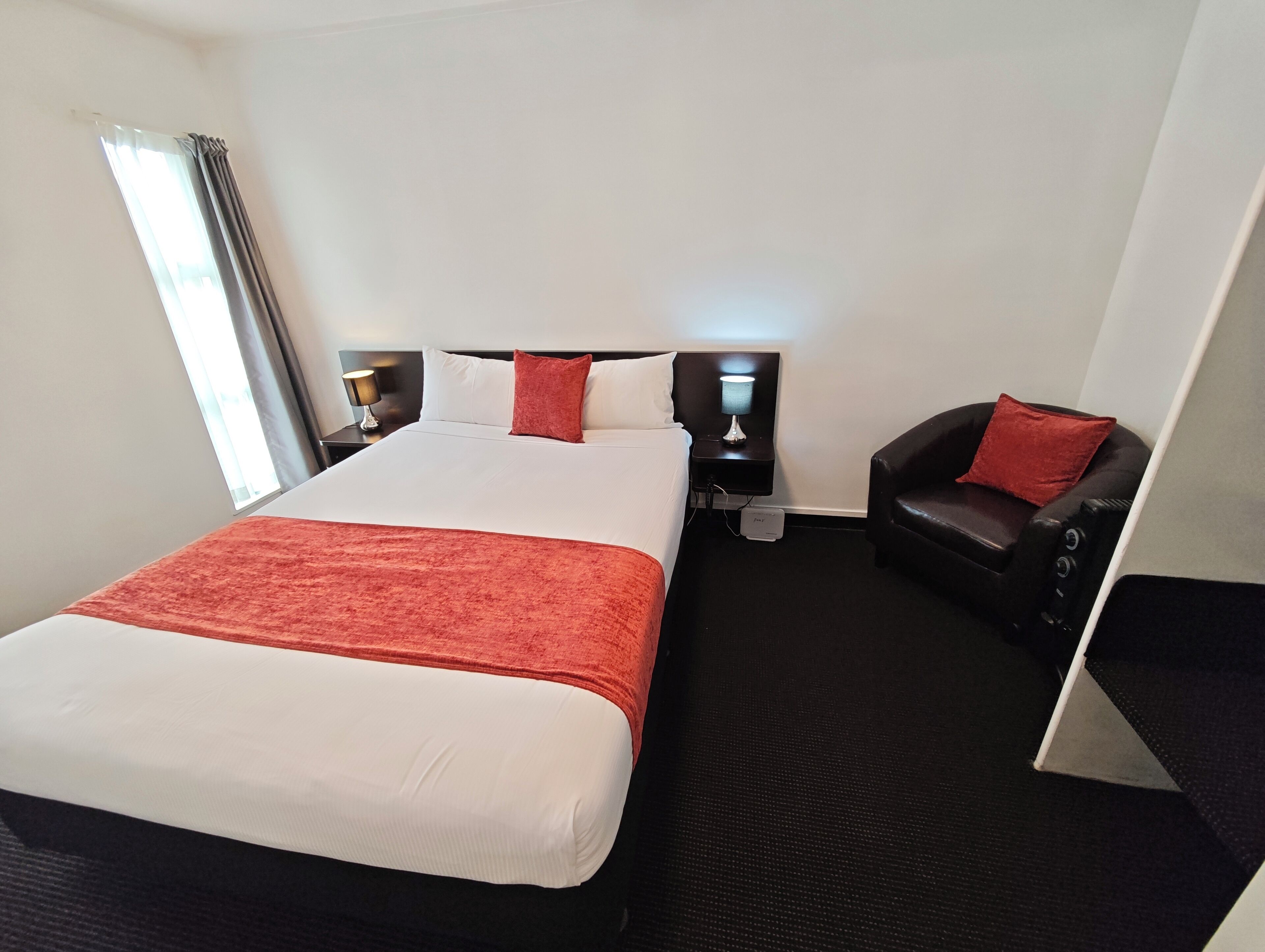Ein Hotelzimmer mit einem großen Bett, zwei Nachttischen mit Lampen, einem Massagesessel und einem Fenster mit Vorhängen.