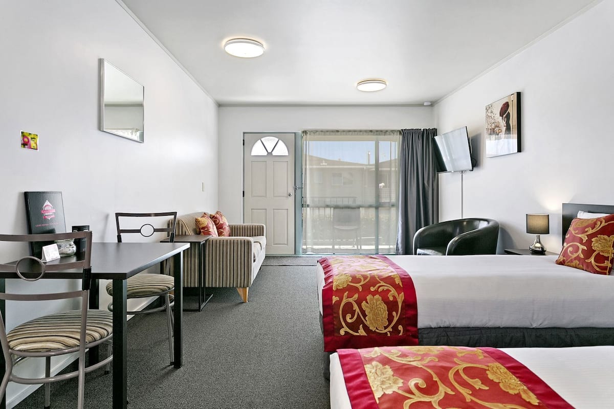 Une chambre d’hôtel équipée d’un bureau, de deux lits, d’une chaise, d’une télévision et d’une fenêtre donnant sur un paysage agréable.