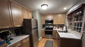 A compact kitchen with wooden cabinets, stainless steel appliances, and a window with blinds.