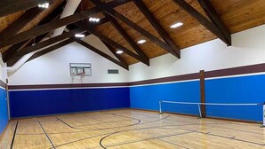 An indoor sports hall with a basketball court, wooden beams on the ceiling, and blue walls.