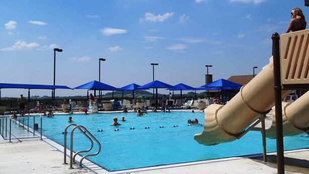 A swimming pool with blue umbrellas, a slide, and people swimming.