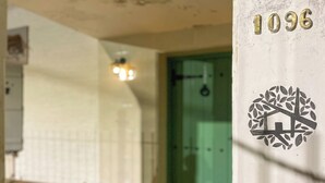 A building entrance with a green door, a number '1096' on a white wall, and a circular emblem with a house and leaves. - Casa del Árbol Hostel (Concepción del Uruguay)