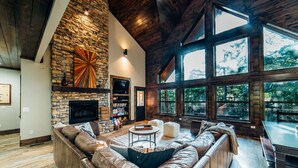 Un salón amplio con chimenea de piedra, sofás de cuero y ventanas grandes que ofrecen vistas al exterior.