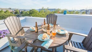 Une table ronde en bois, entourée de chaises, avec des bouteilles et des assiettes, sur une terrasse en toit offrant une vue sur la ville.