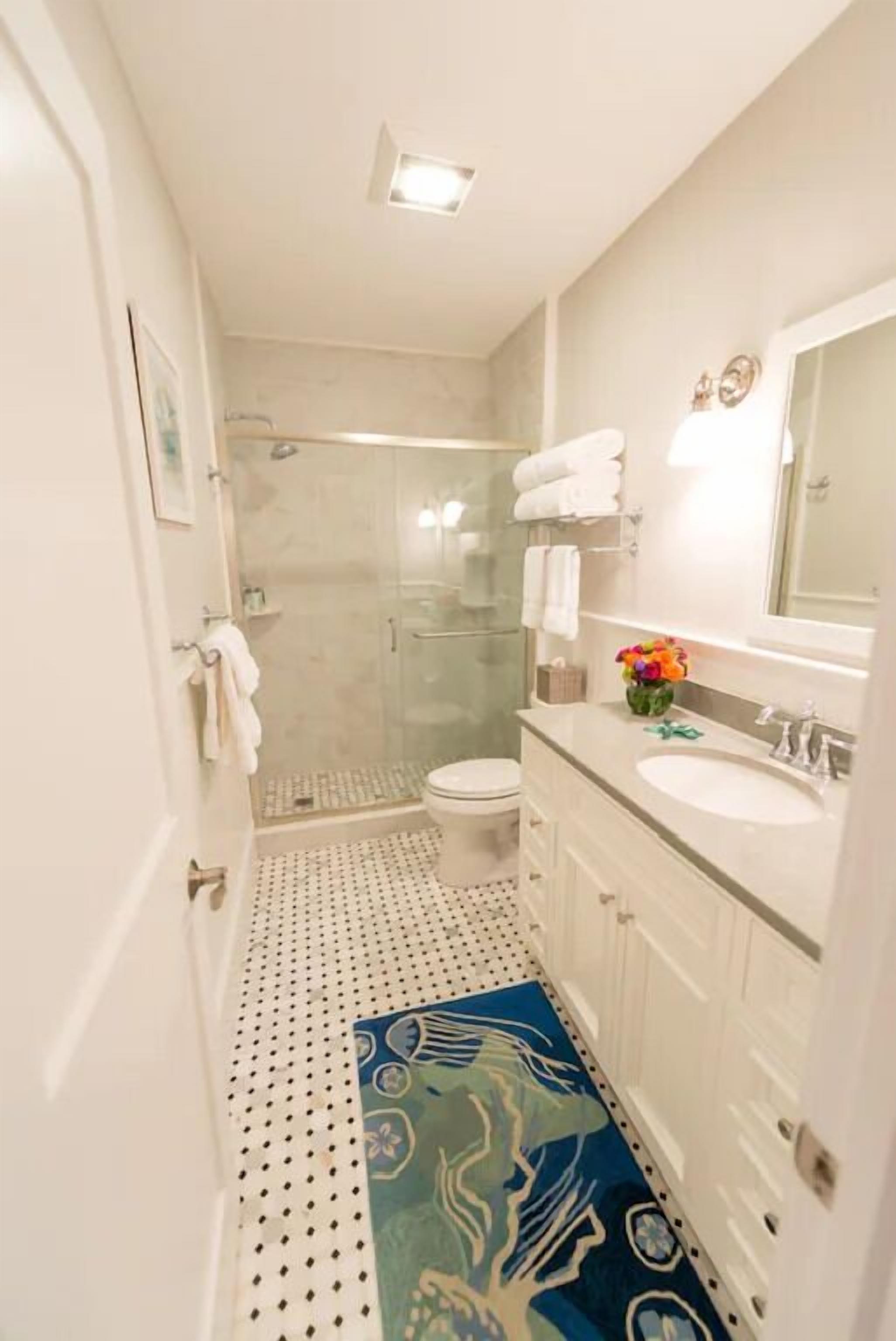 A bathroom with a shower, toilet, sink, and mirror.
