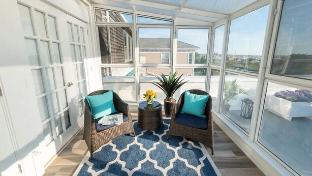 Une véranda avec deux fauteuils en osier, un tapis à motifs bleus et une plante en pot.