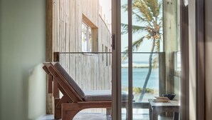 A wooden-framed balcony with a single lounge chair, a small table, and a view of the ocean and palm trees. - Casa Uca (Camocim)
