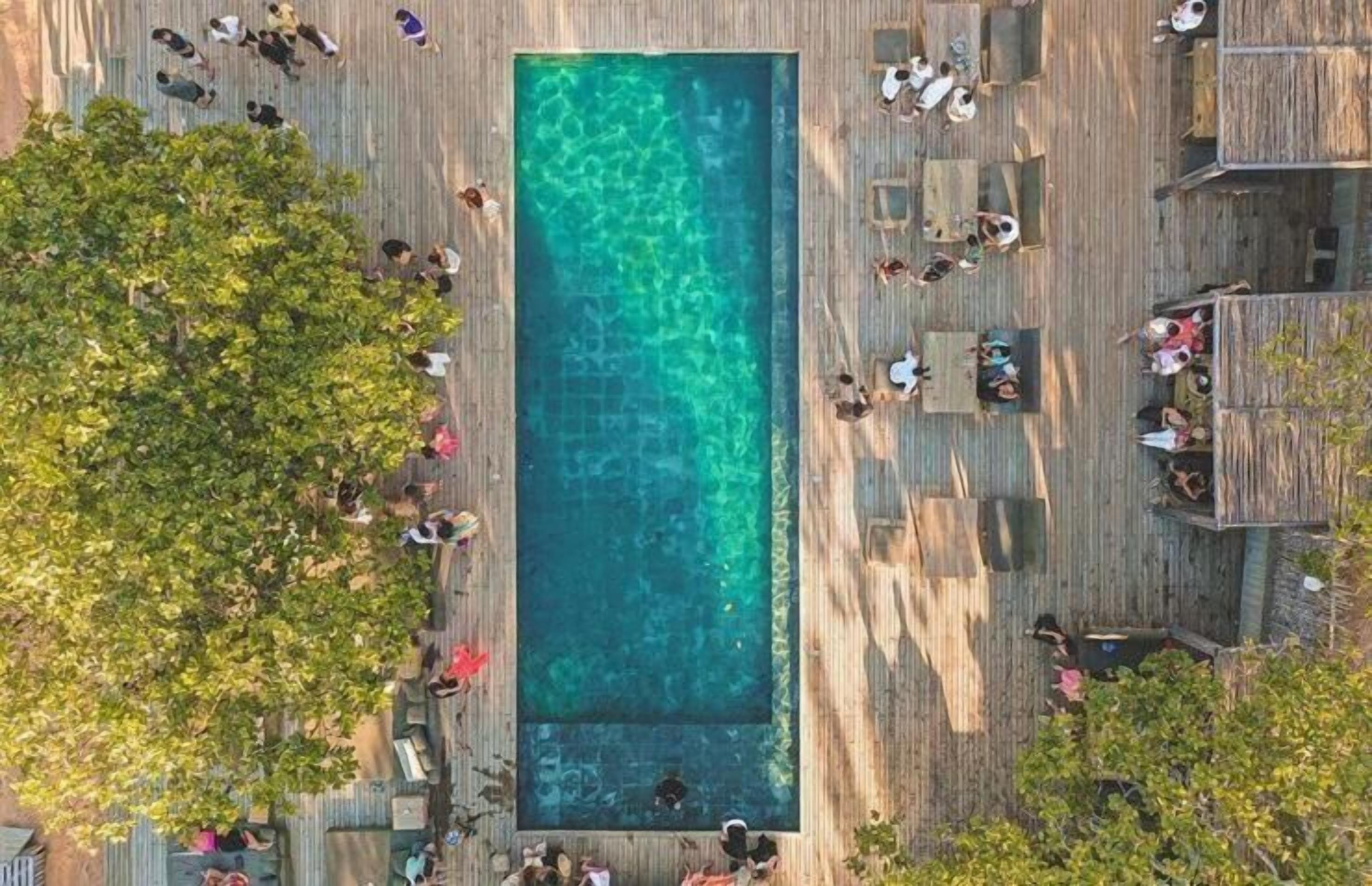 Vista aérea de una piscina rectangular rodeada de terrazas de madera con gente.
