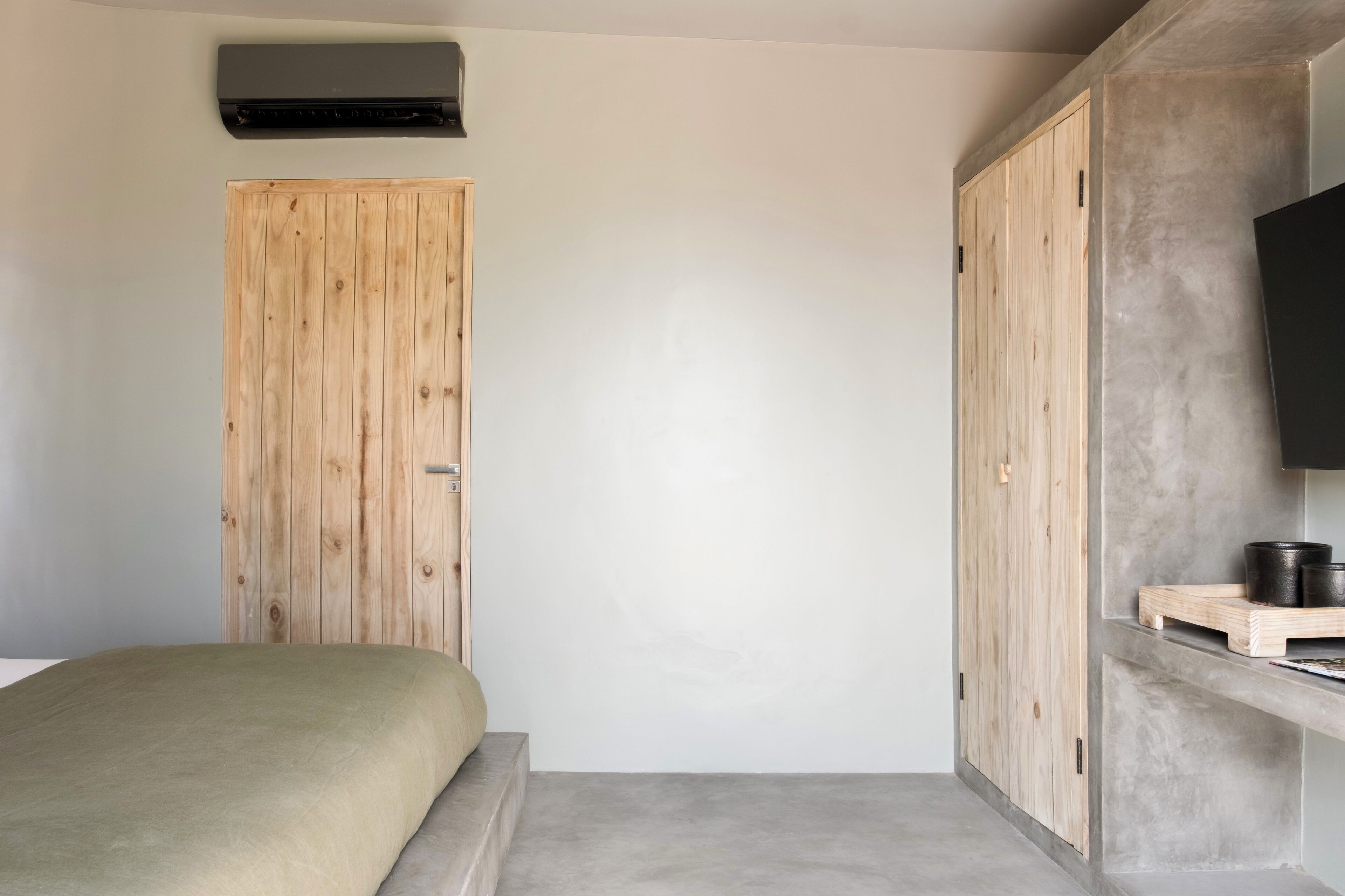 A bedroom with a bed, a wooden wardrobe, a television on a stand, and a small shelf with items.