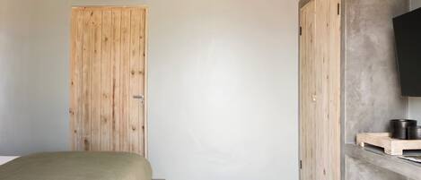 A bedroom with a bed, a wooden wardrobe, a television on a stand, and a small shelf with items.