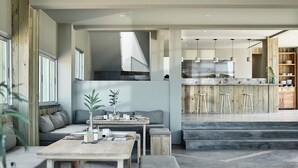 A modern kitchen with wooden accents, a dining area with a sofa and table, and a bar area with stools. - Casa Uca (Camocim)