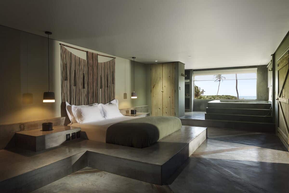 Un dormitorio moderno con una cama grande, cabecera de madera y vista al océano a través de un ventanal amplio.