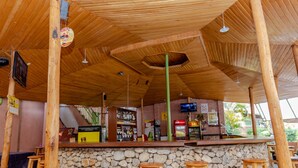 Un rústico área de bar con vigas de madera, pared de piedra y taburetes de madera.