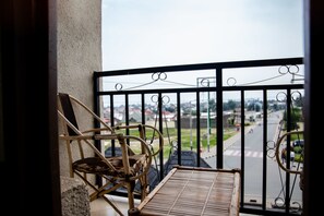 Un balcón con vista a una calle y casas. Hay dos sillas de mimbre y una mesita.