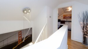 A modern interior with a staircase, a wall-mounted light fixture, and a view into a kitchen area. - 5* Luxury Spacious Apartment (Mitcham)