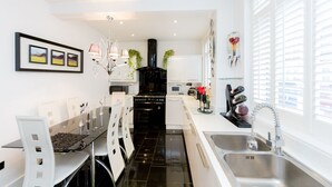 A modern kitchen with a black stove, white cabinets, and a stainless steel sink. There are framed pictures on the wall and a chandelier above the dining table. - 5* Luxury Spacious Apartment (Mitcham)
