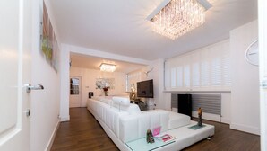 A modern living room with a white sofa, a glass coffee table, a fireplace, and a television. - 5* Luxury Spacious Apartment (Mitcham)