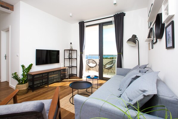 Ein modernes Wohnzimmer mit einer Couch, einem Fernseher, einem kleinen Tisch und einer Pflanze.