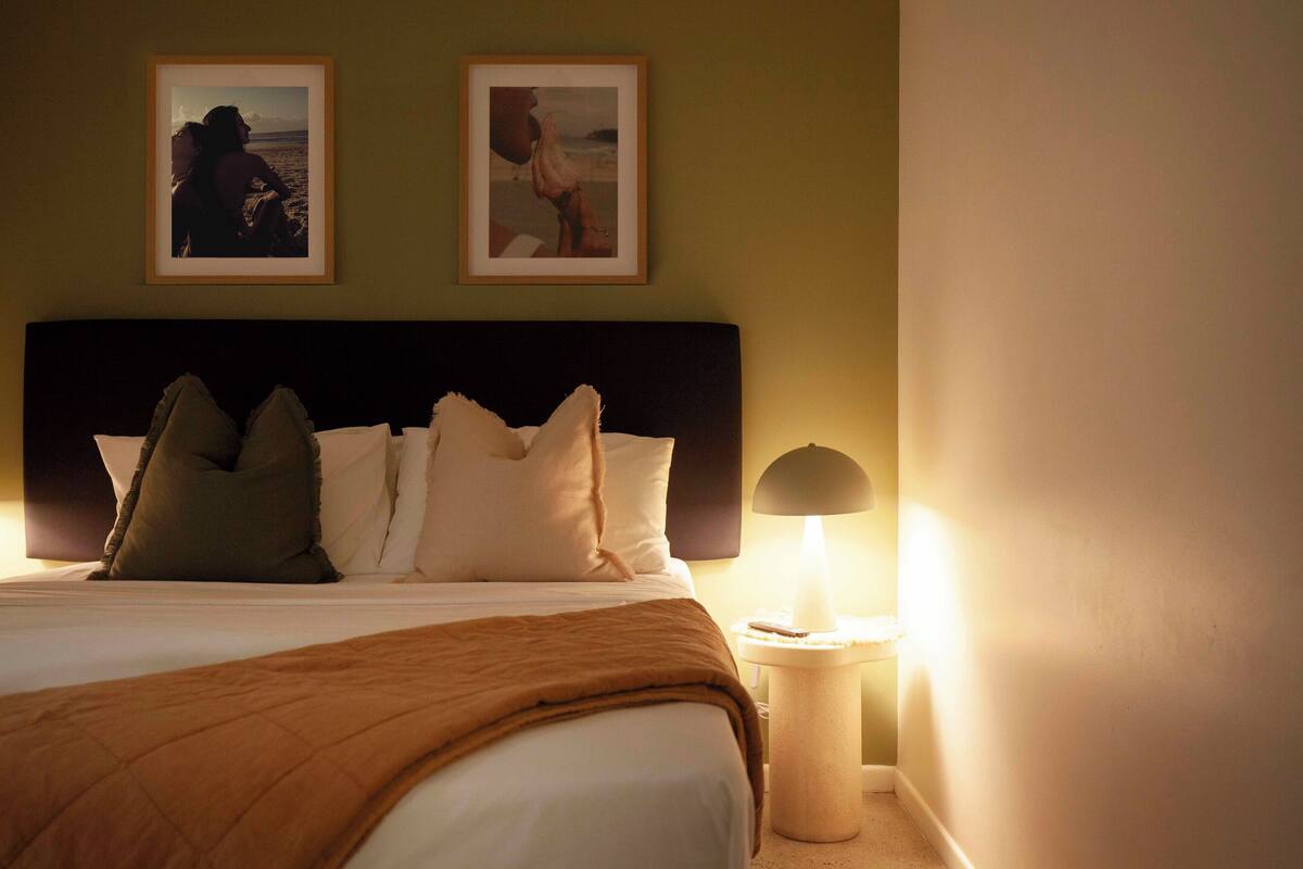 A neatly made bed with a brown blanket, a bedside lamp, and two framed pictures on the wall.