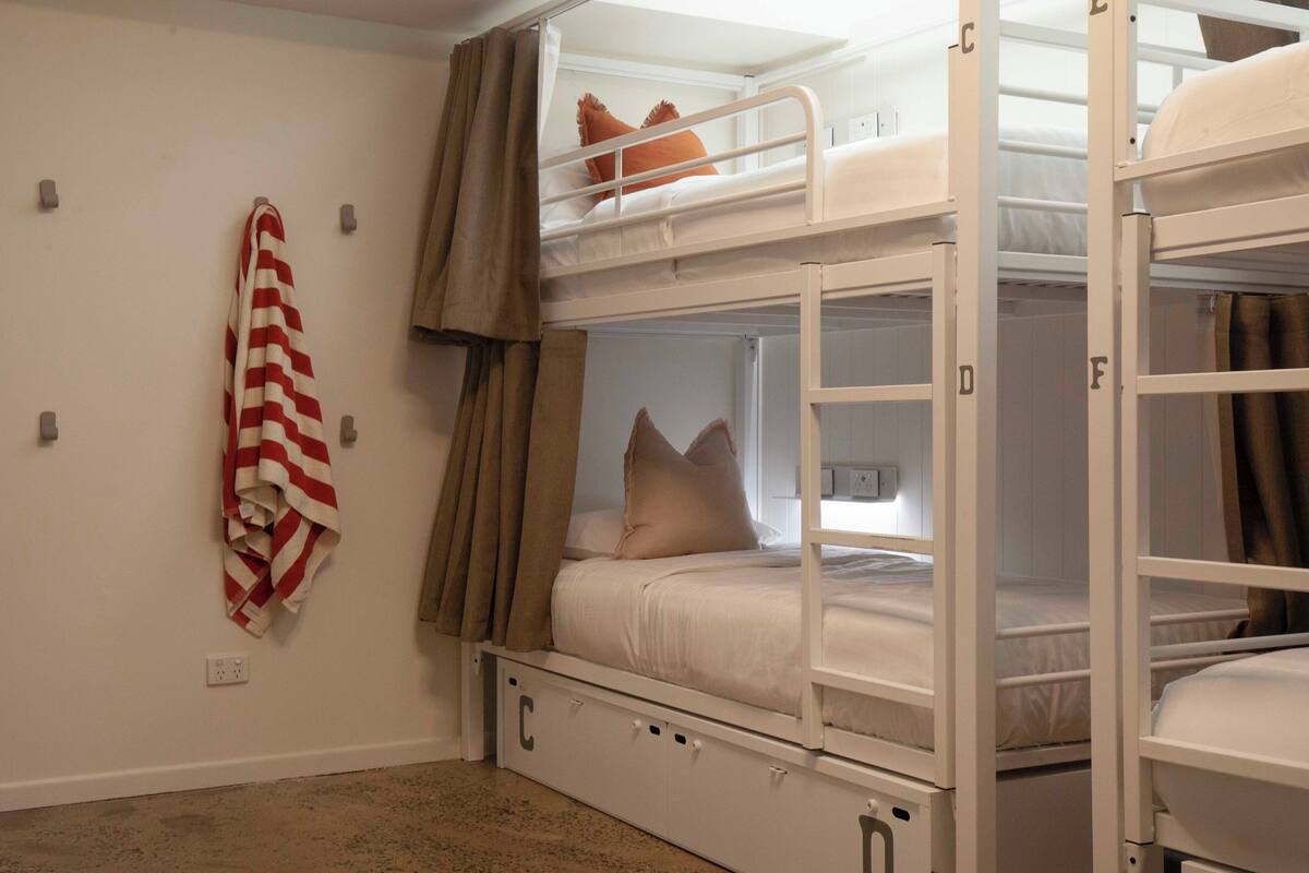 A bunk bed room with a striped towel on the wall, a window with curtains, and a power outlet.