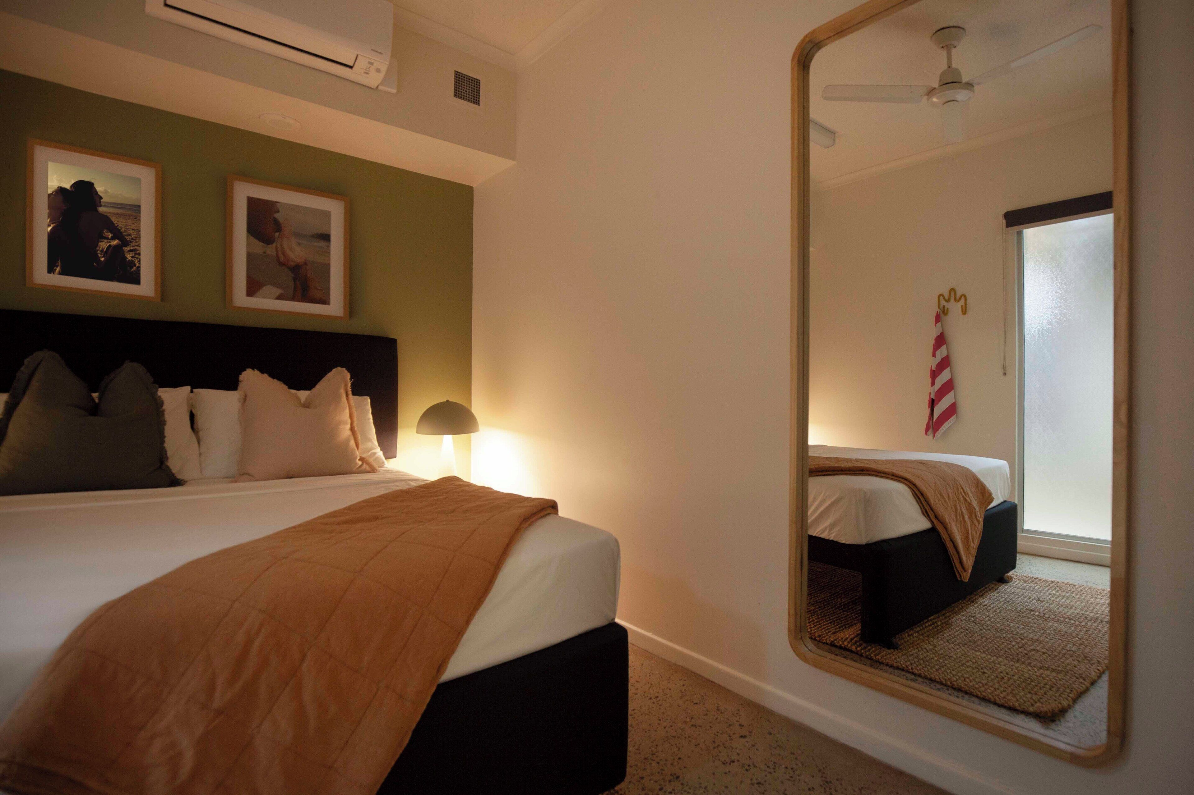 Une chambre d’hôtel avec un lit, une lampe de chevet, un miroir et deux tableaux encadrés au mur.