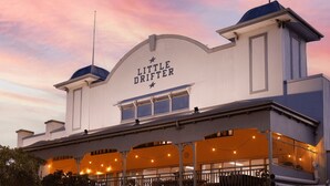 Un edificio con un letrero que dice "Little Drifter" y un área de estar al aire libre techada con luces colgantes.