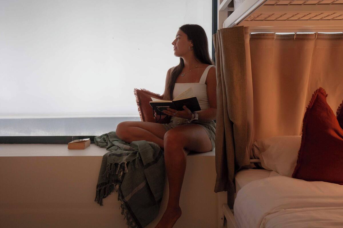 A person sitting on a window sill reading a book.
