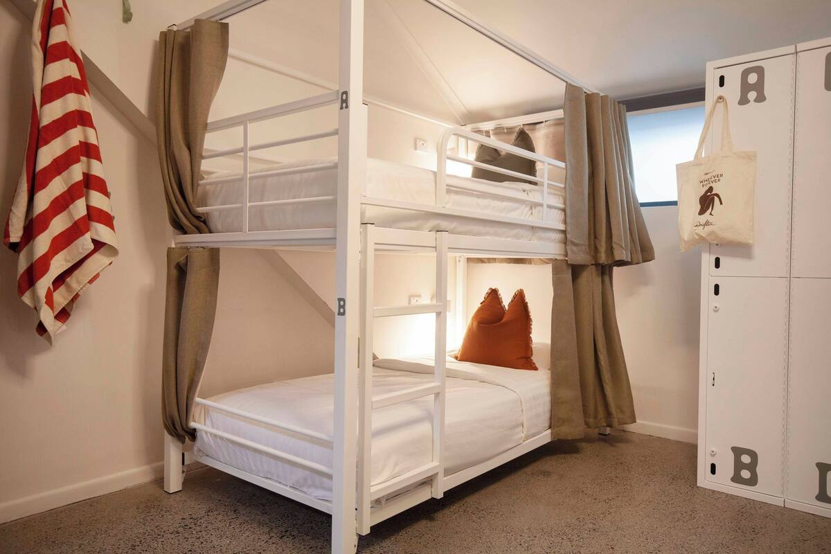 A bunk bed room with a striped towel, brown curtains, and a storage unit with letters.