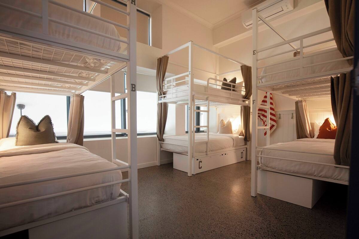 A room with bunk beds, a window with curtains, and a bed with a striped pillow.