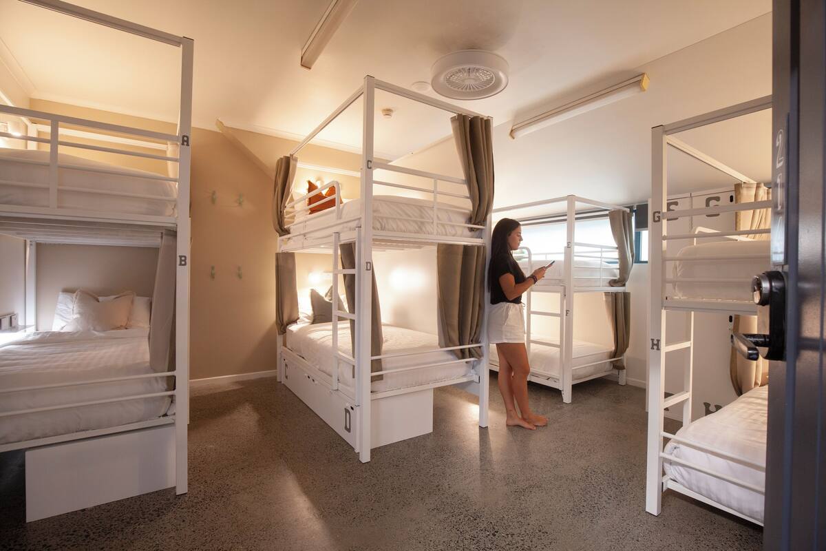A dormitory room with bunk beds, a ceiling fan, and a window with curtains.