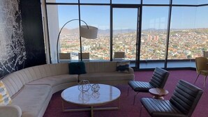 A modern living room with a curved sofa, a round coffee table, and two leather armchairs. Large windows offer a city view. - Loft Style Condo with Stunning View of Tijuana (Tijuana)
