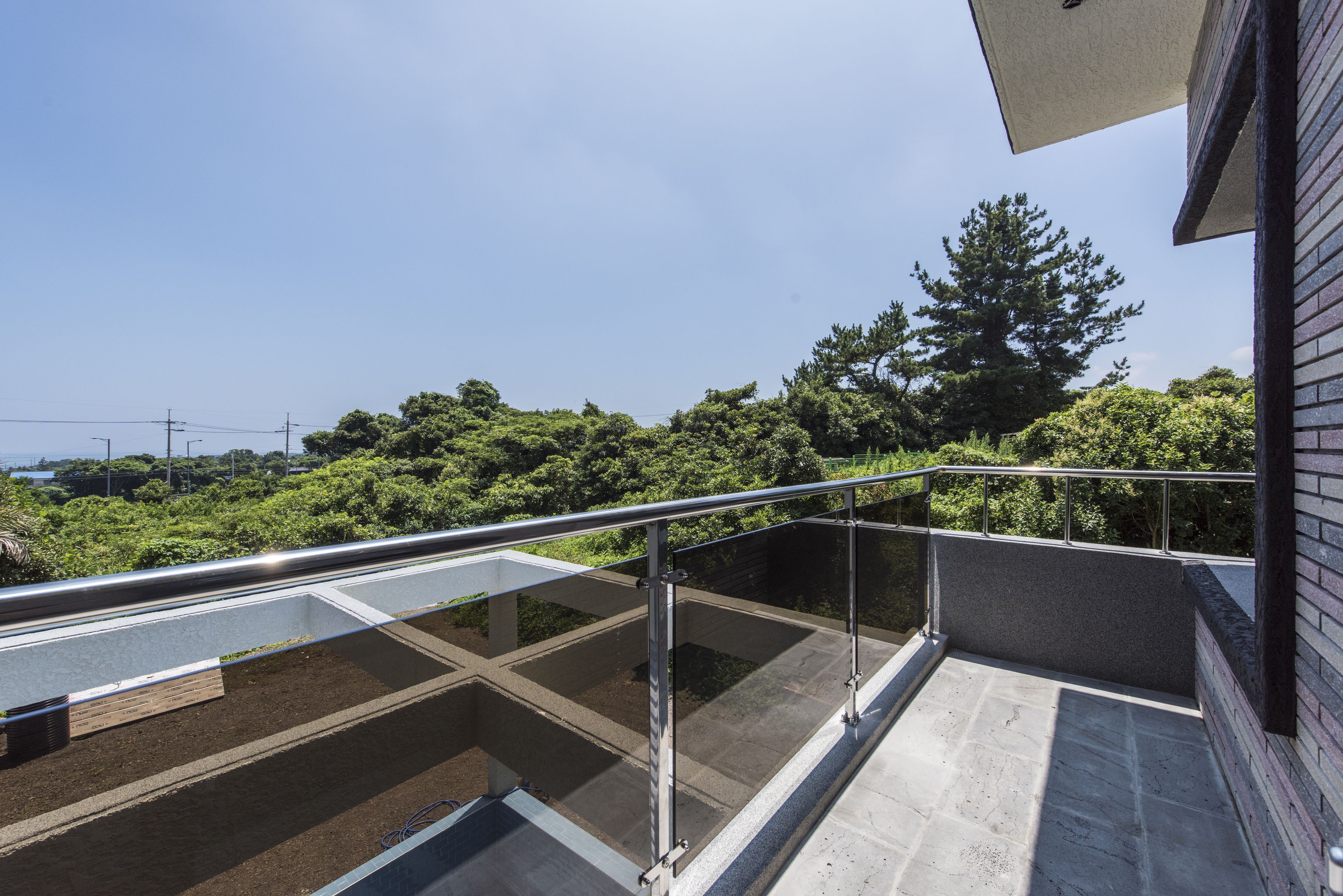 A rooftop terrace with a glass floor, metal railing, and a view of dense greenery.