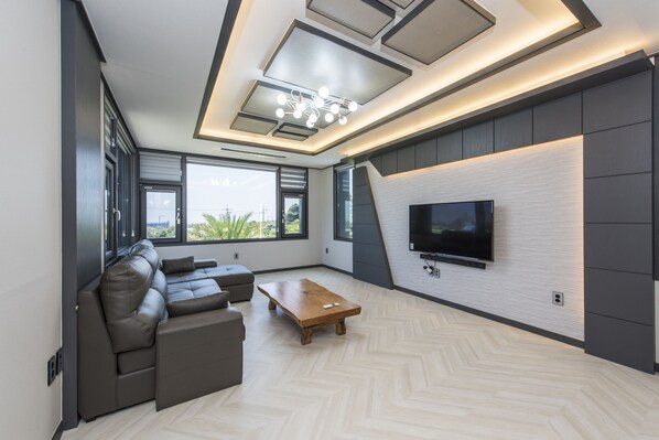 A modern living room with a sectional sofa, a wooden coffee table, and a flat-screen TV mounted on a textured wall. - The Some Plus Onpyeong (Seogwipo)