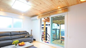 A modern living room with a sofa, a coffee table, and a view through a glass door to an outdoor area. - Tramonto Pension (Seogwipo)