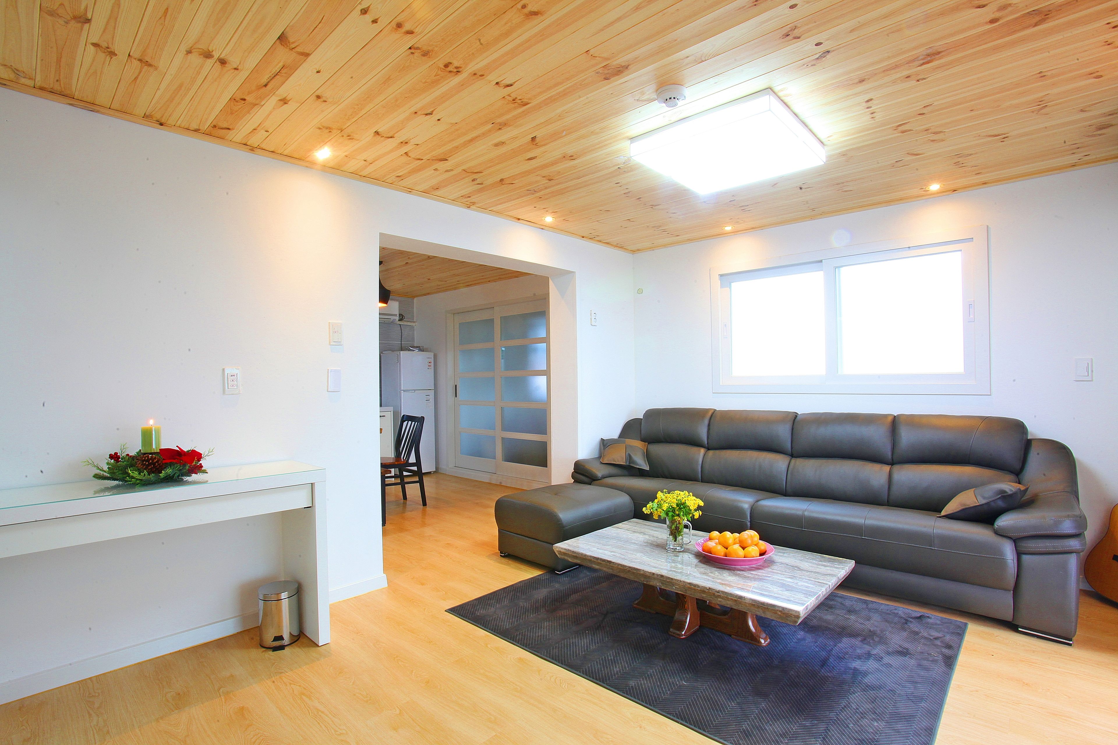 Una sala de estar moderna con techo de madera, un sofá gris, una mesa baja con flores y una mesa de vidrio con una vela.
