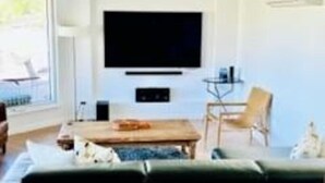 Un salon moderne avec un grand téléviseur à écran plat fixé au mur, un canapé de couleur foncée, une table basse en bois et une table d’appoint avec un plateau en verre.