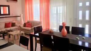 Una sala de estar moderna con sofá, sillones, una mesa de comedor con sillas y un televisor montado en la pared.