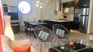 Una sala moderna con una mesa de centro de vidrio, dos sillas de mimbre, un sofá y un comedor con una mesa redonda y sillas.